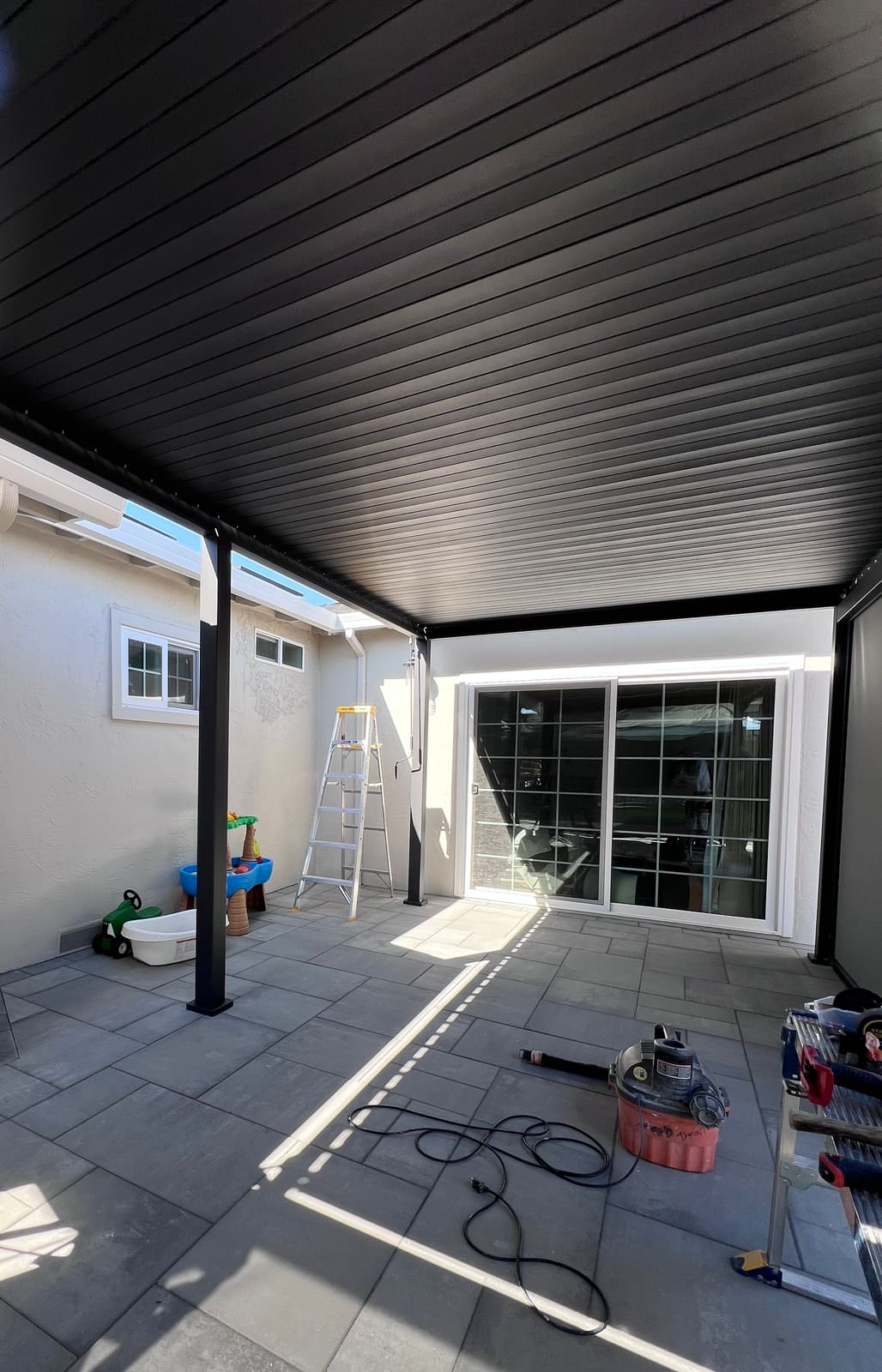 Patio cover after installation — sleek black louvered ceiling over a tiled patio with completed dark finish