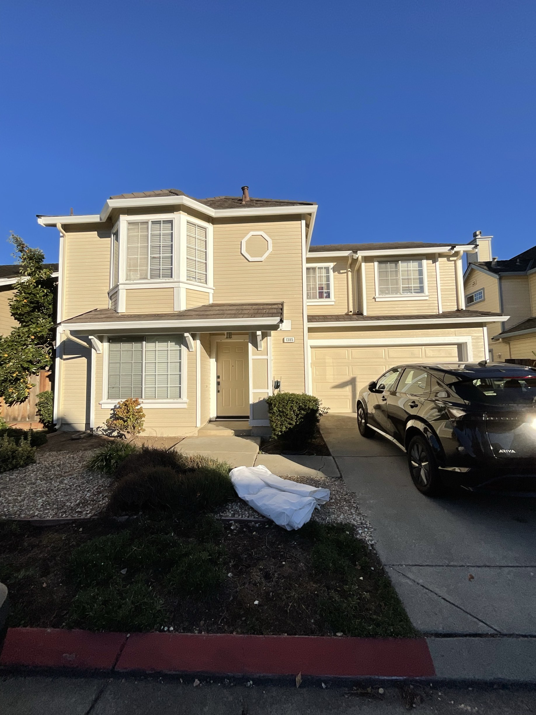 Two-story home repainted in warm cream-yellow with crisp white trim under a bright blue sky