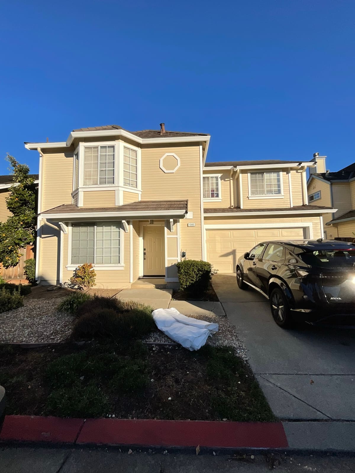 Two-story home repainted in warm cream-yellow with crisp white trim under a bright blue sky